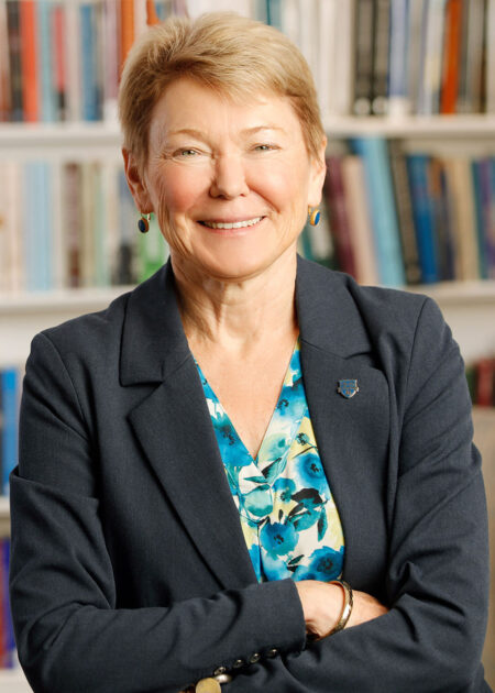 Sarah Mangelsdorf smiling at the camera with her arms crossed with bookshelves behind her.