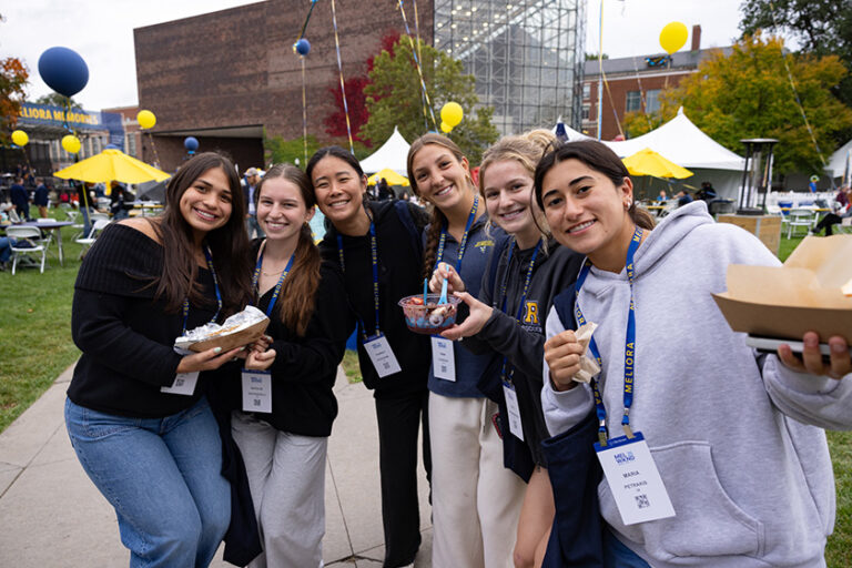 Young alumnae smile for the camera while holding their food truck meals outside of Wilson Commons.