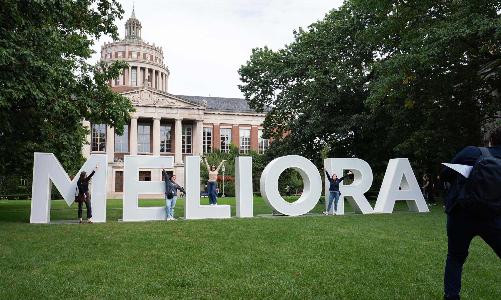 Alumni pose on and with the giant MELIORA letters on the Eastman Quad.