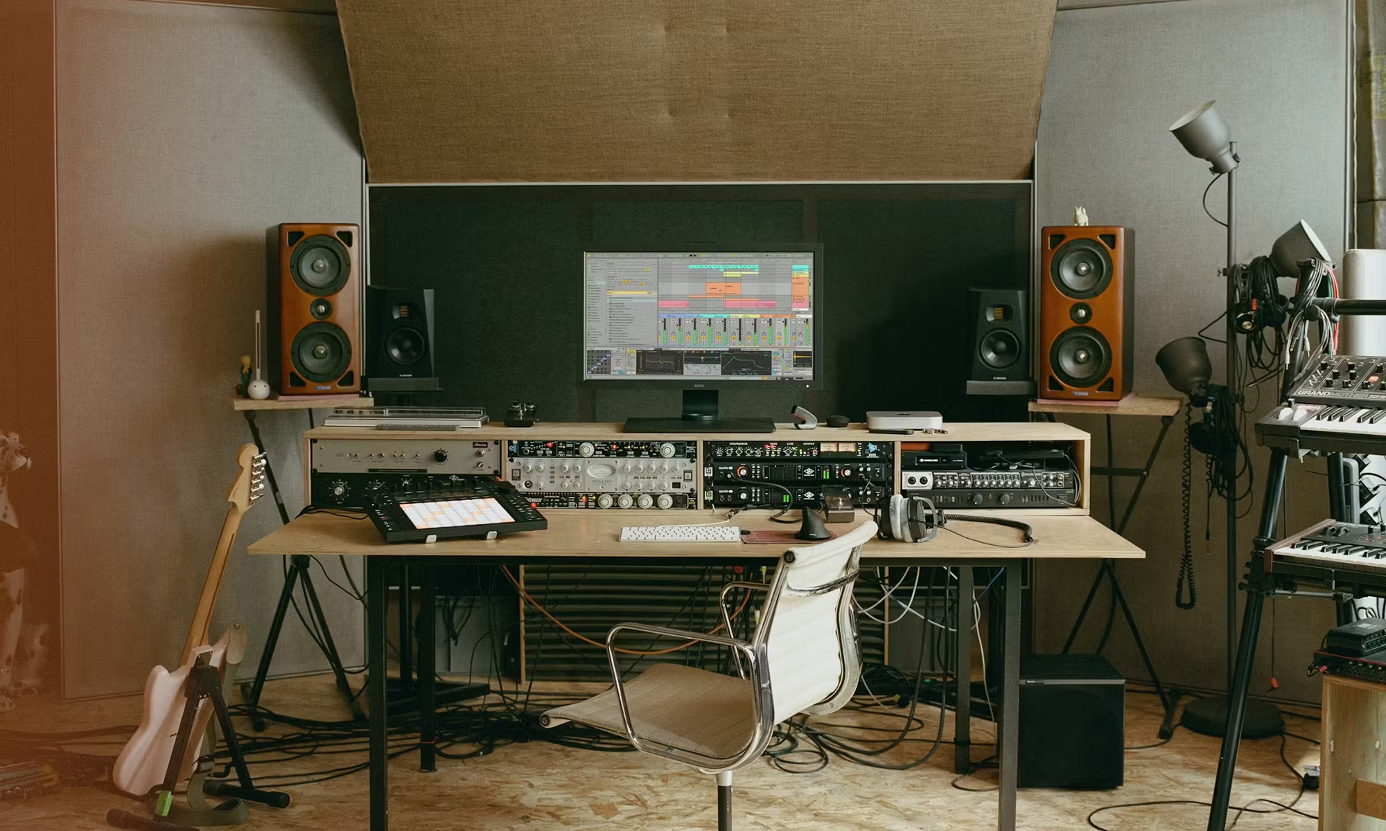 A digital audio workstation with a computer monitor running digital audio software, audio equipment, speakers, keyboards, and a guitar.