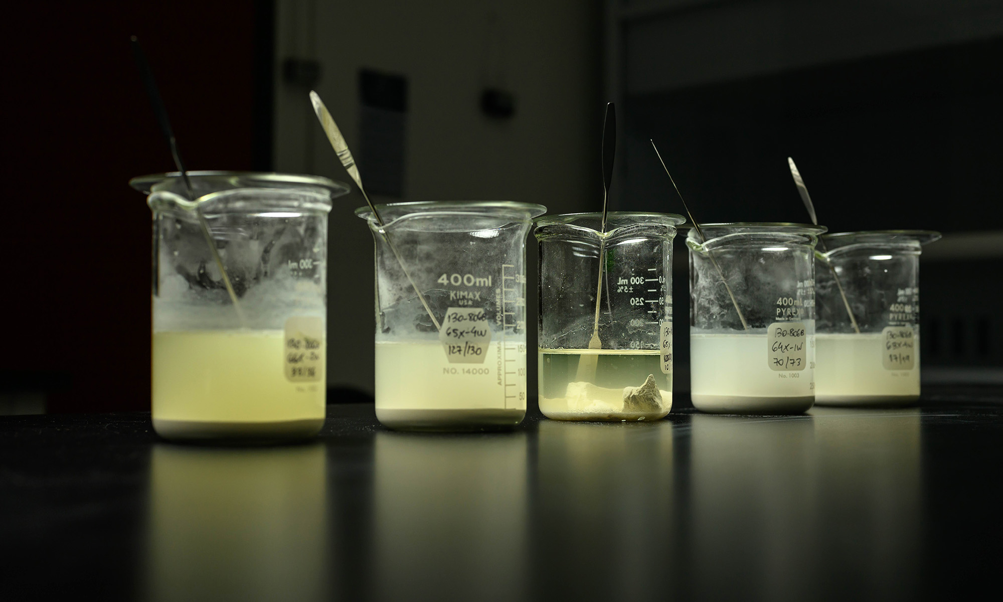 Five beakers filled sediment samples containing foraminifera microfossils soaking in cloudy water to loosen and disaggregate material.