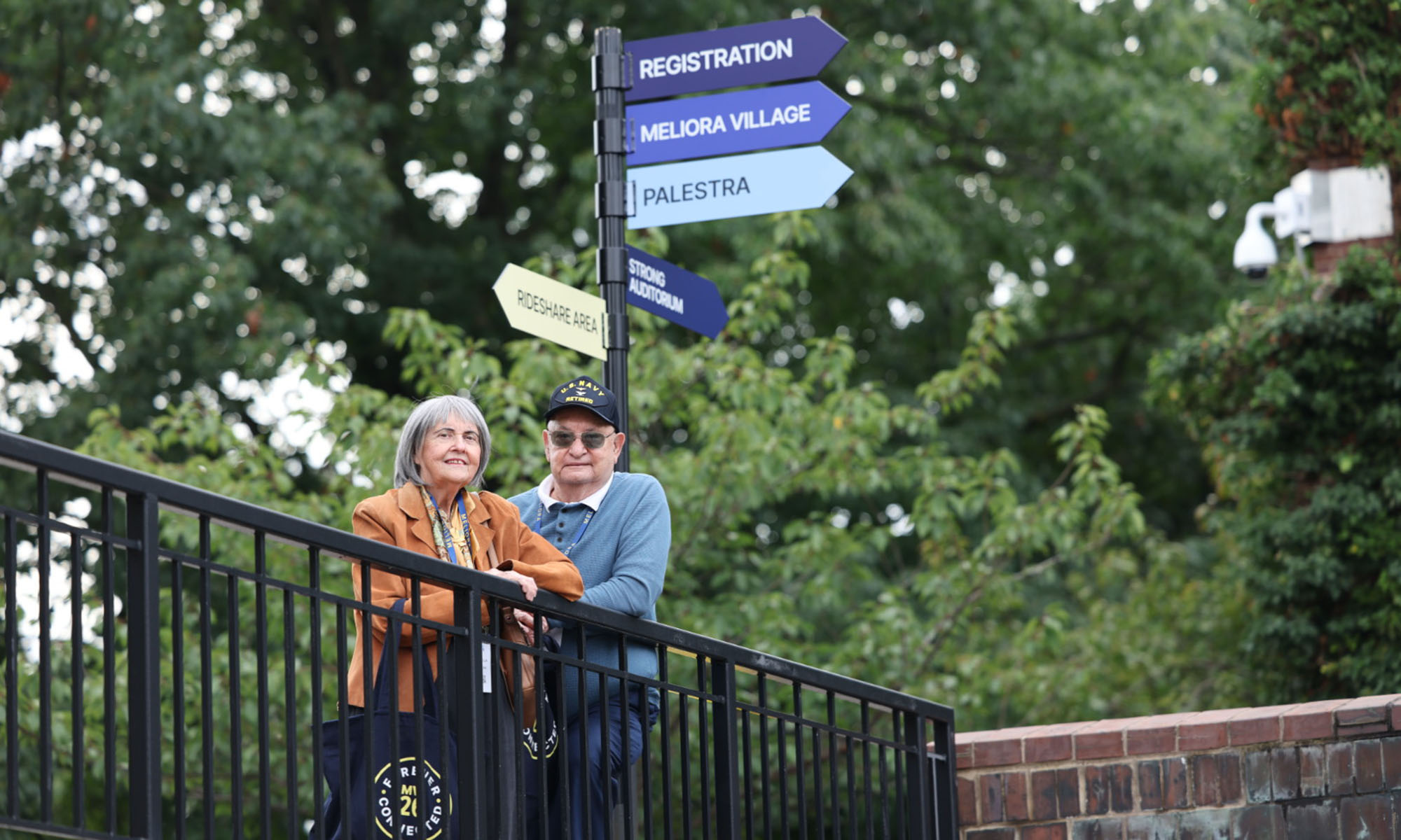 Matthew Klocek and his wife, Priscilla, smile for a photo near the Meliora Weekend wayfinding signs.