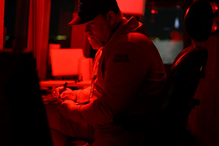 A researcher works with scientific equipment under red lighting aboard the R/V Blue Heron.
