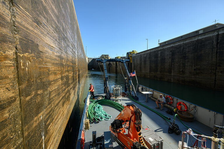 The research vessel Blue Heron passes through a narrow lock in the Welland Canal, surrounded by high concrete walls.