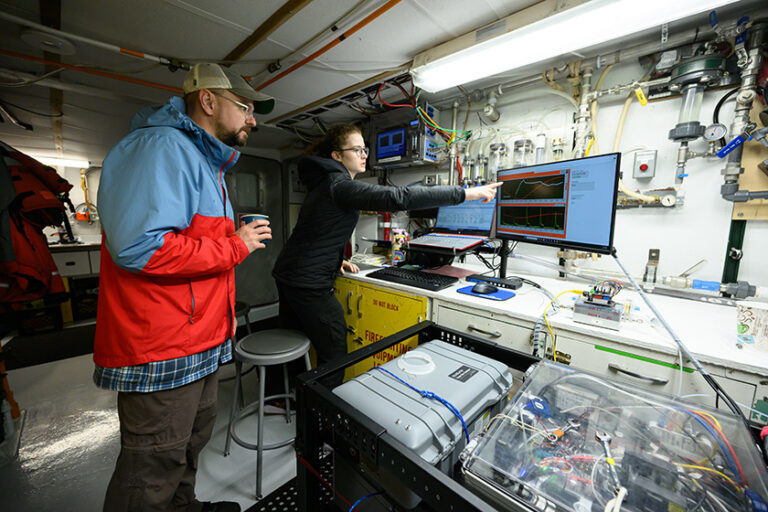 John Kessler and Rebecca Rust examine computer monitors and equipment inside the R/V Blue Heron.