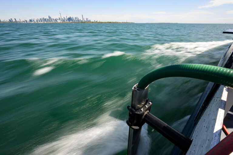 A green hose extends into the choppy waters of Lake Ontario from the R/V Blue Heron.