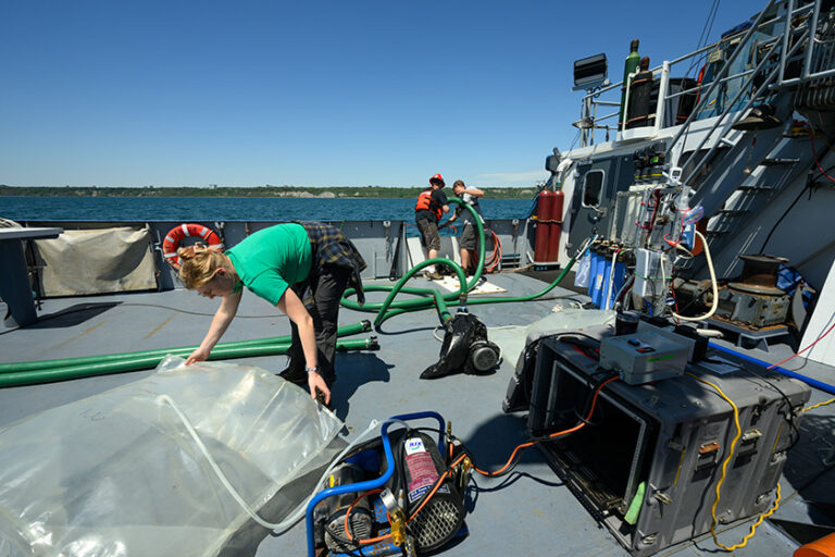 Rachel Flickinger bends over a large plastic gas-collection pouch on the deck of the R/V Blue Heron.