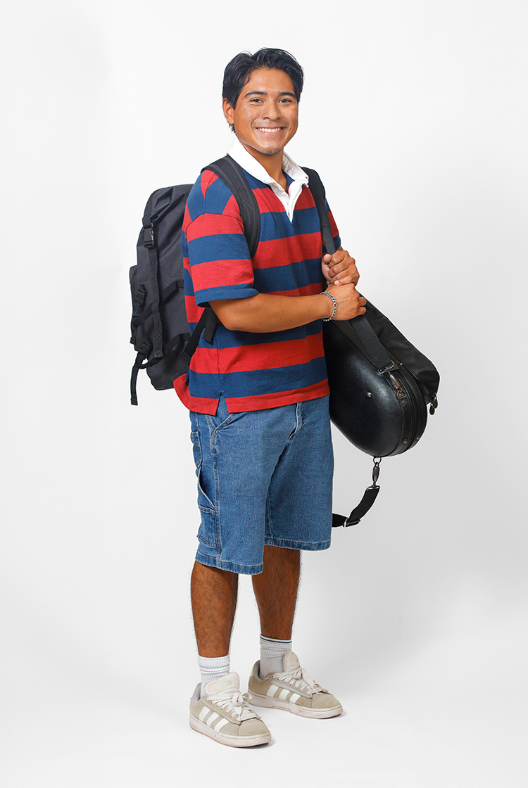 Alexnader Hatch in a rugby shirt with a white collar and red and blue stripes, knee-length denim shorts, and sneakers with a black backpack and a black instrument case.