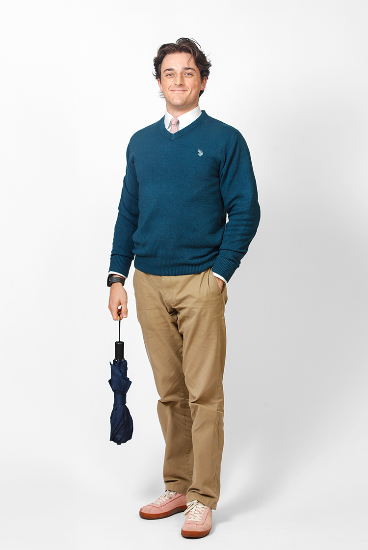 Elijah Gebers in khaki-colored slacks, a teal sweater vest over a colored shirt and tie, with pink shoes, and holding an umbrella.