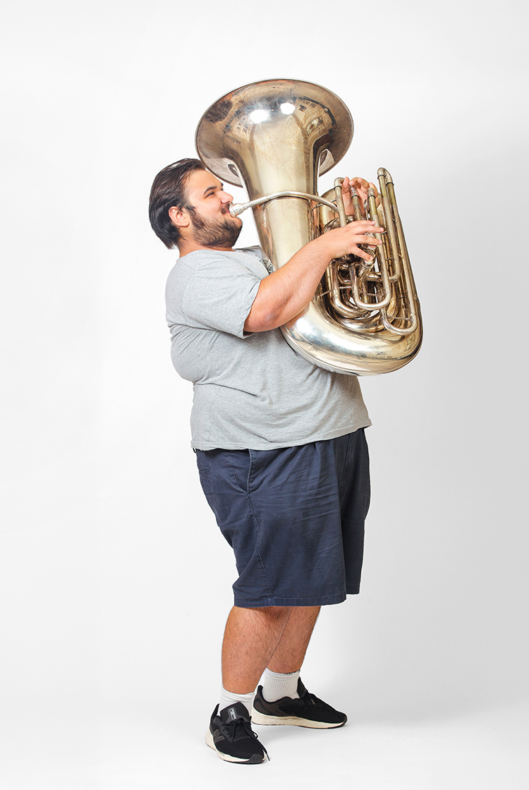 Matthew Langrell in shorts and a gray t-shirt plays the tuba.