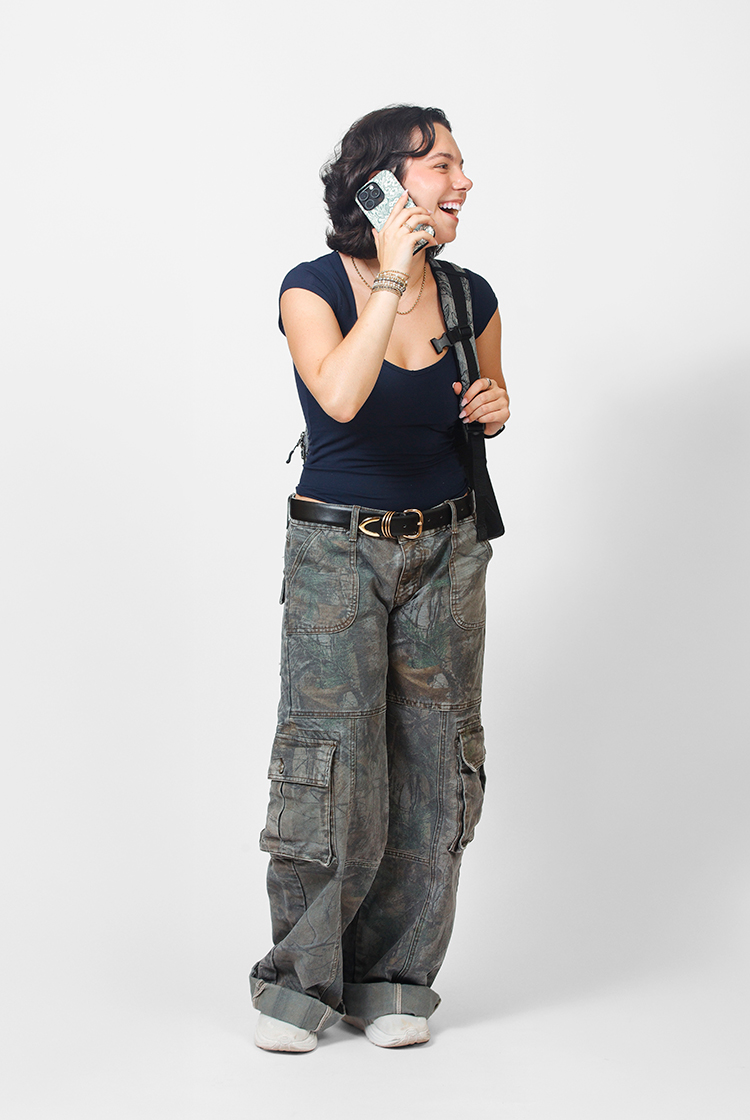 Naomi Chad in white shoes, fatigue-patterned cargo pants, a black t-shirt, takes a phone call.