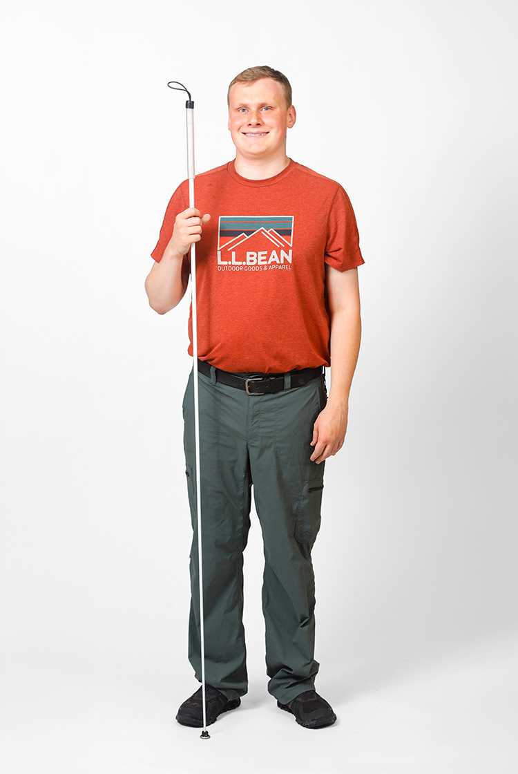 Noah Tobias Carver in gray cargo pants, an orange, short-sleeve L.L. Bean t-shirt, and a white cane.