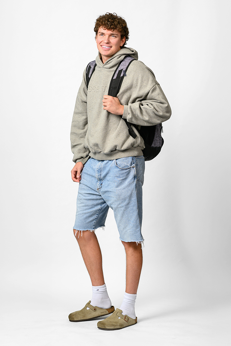 Camden Fleming in a gray hoodie, cutoff jean shorts, clogs with crew socks, and a backpack.