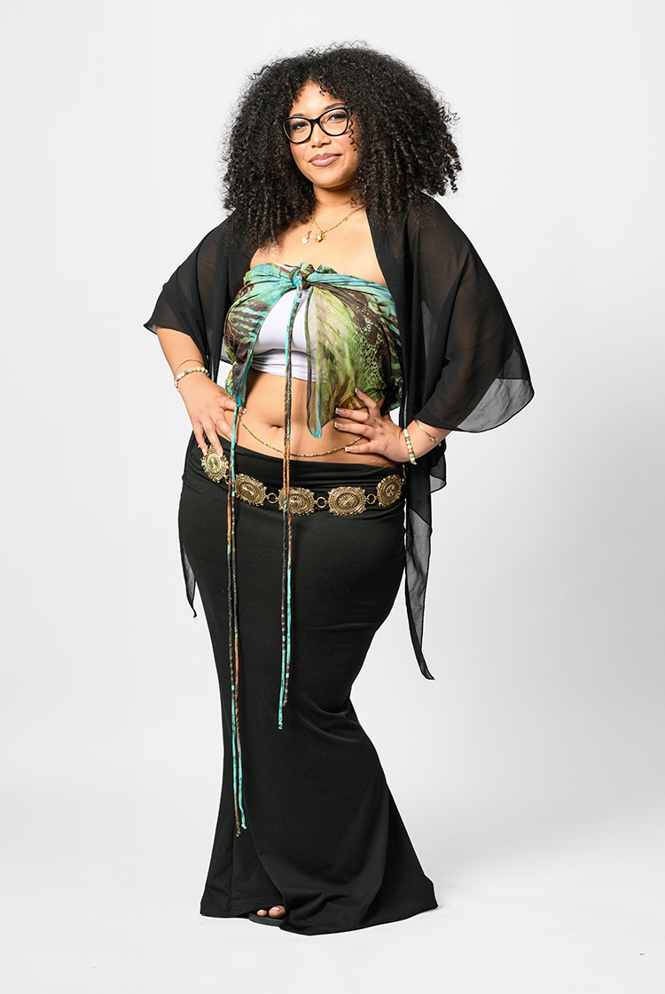 Jai'Neya Wright in a white crop top with a green and blue scraf over it and black shoulder coverup plus black pants with a metalic belt.