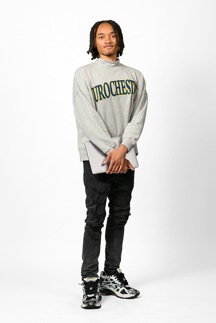 Zakeem Wooten in a gray URochester sweatshirt, black jeans, and sneakers holds a laptop.