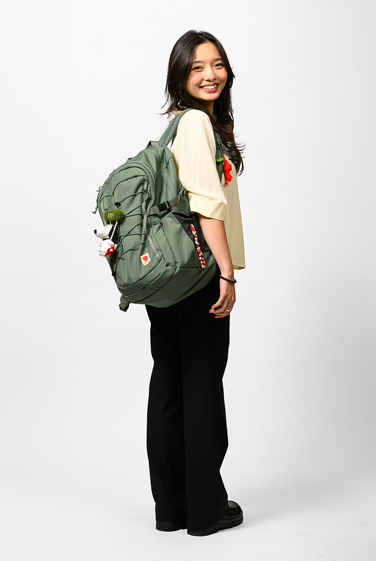 Chloe Wen in dark slacks and a dream top shoes off her green backpack with a Snoopy bag tag.
