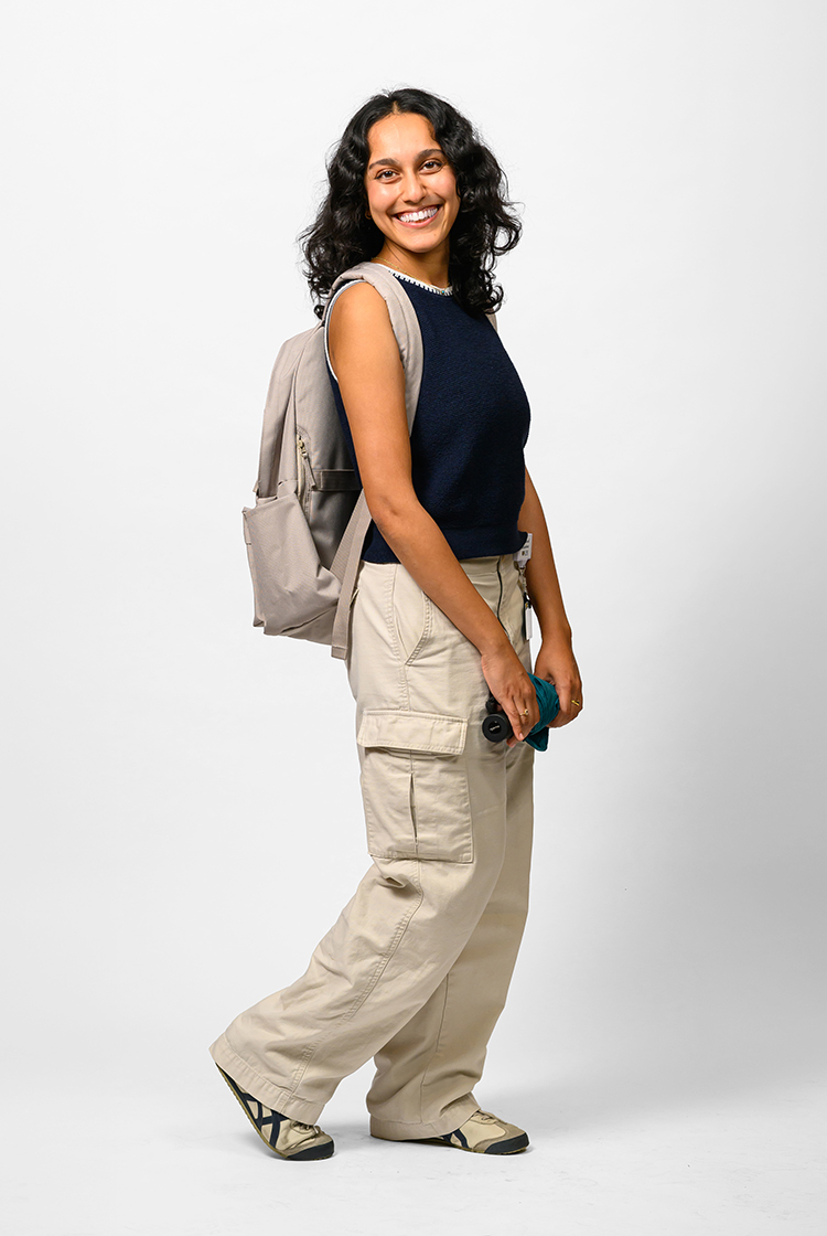 Vrinda Modi in a black tank, khaki cargo pants, white and black shoes, and with a gray backpack and an closed umbrella in her hands.