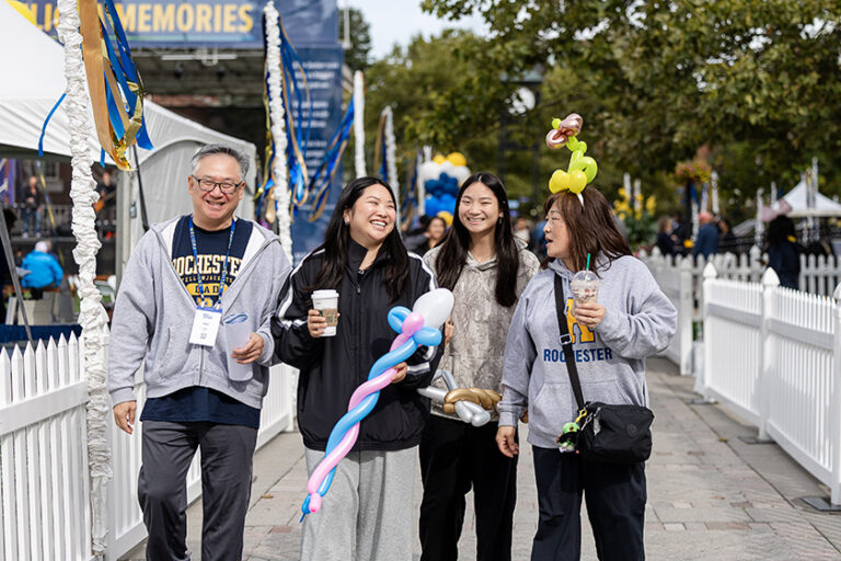 A family of our walks around Meliora Village smiling and laughing with balloons, beverages, and crafts in town.
