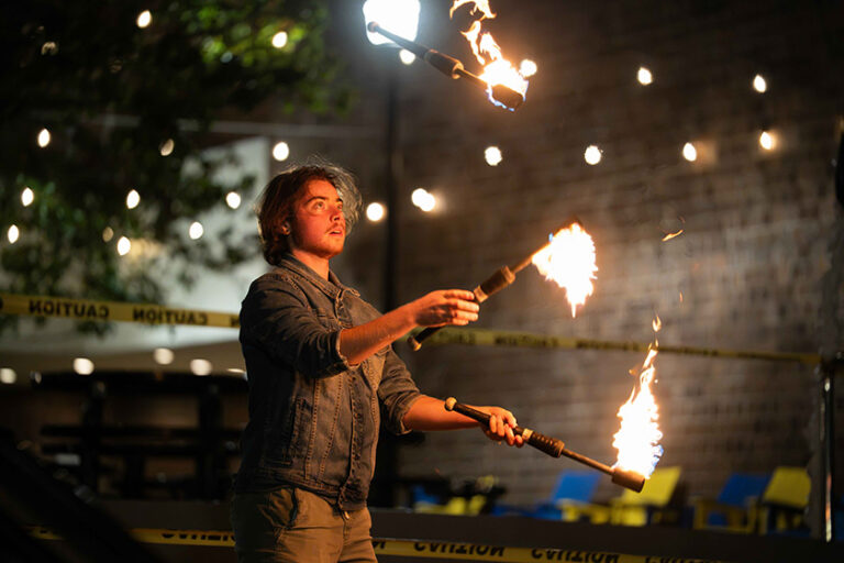 A member of the Strong Jugglers juggles batons alit with flames.