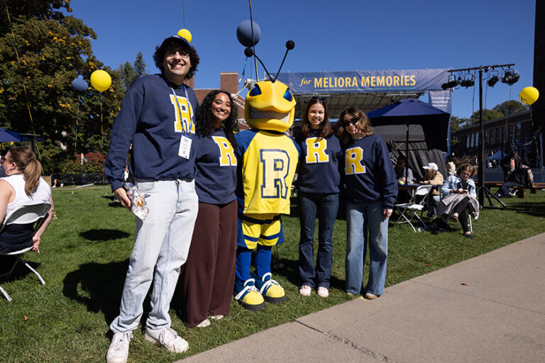 University of Rochester seniors in their blue-and-yellow sweatshirts pose for a photo with mascot Rocky.
