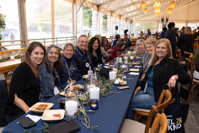 Long view of a table with Meliora Weekend attendees seated at it and smiling for the camera.