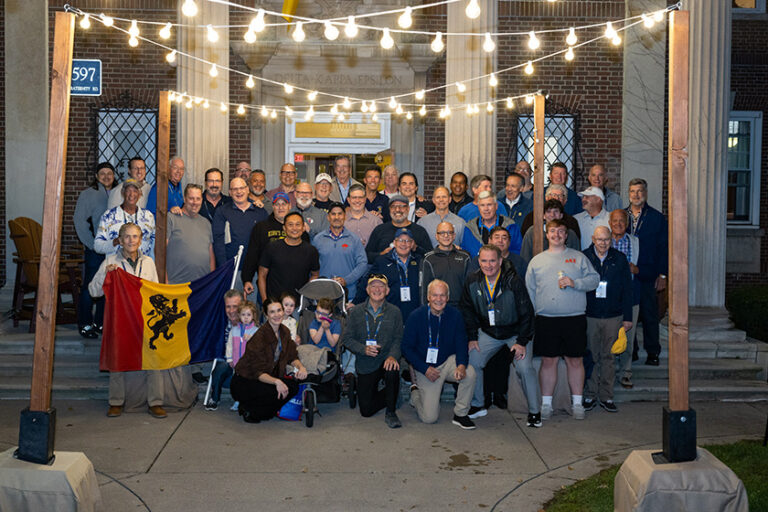 Members current and past of the DKE fraternity pose for a group photo in front of their house in the evening.