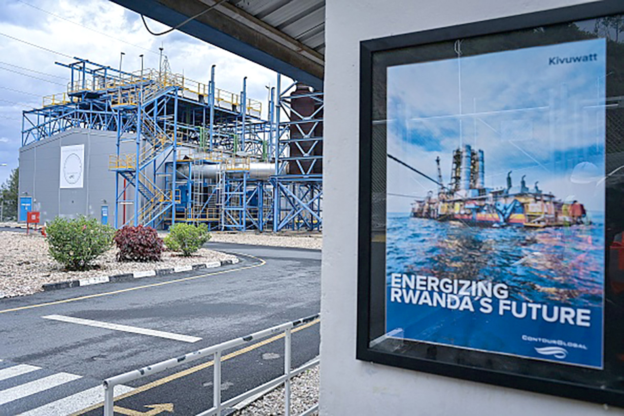 A framed poster on a wall displays an offshore oil platform with the text energizing Rwanda's future, set against an industrial background with metal structures and a paved road.