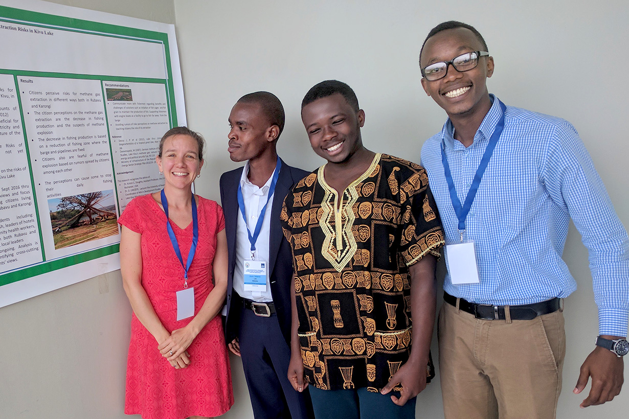 Kristin Doughty poses next to a poster with three colleagues during field research in Rwanda.