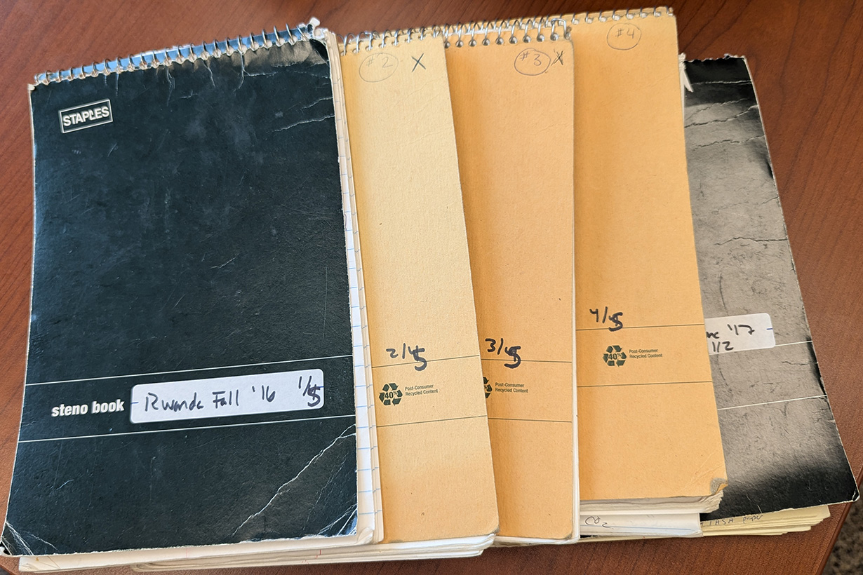 A stack of notebooks rests on a wooden surface, documenting Kristin Doughty's field research.