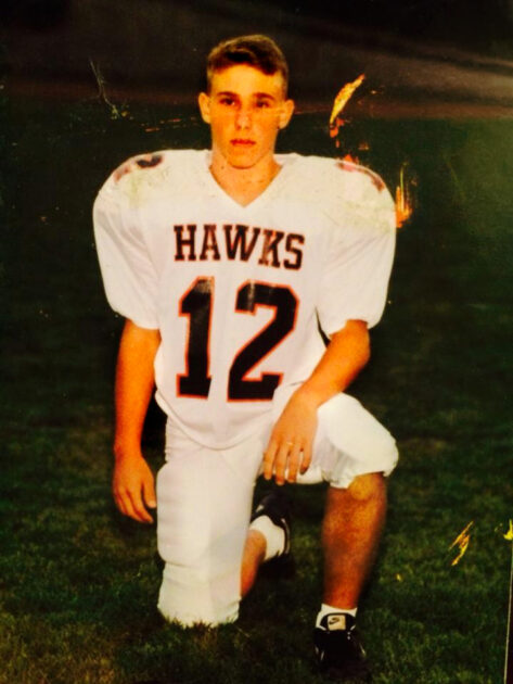A young Rob Lynch kneels on a football field in a white Hawks uniform with the number 12.