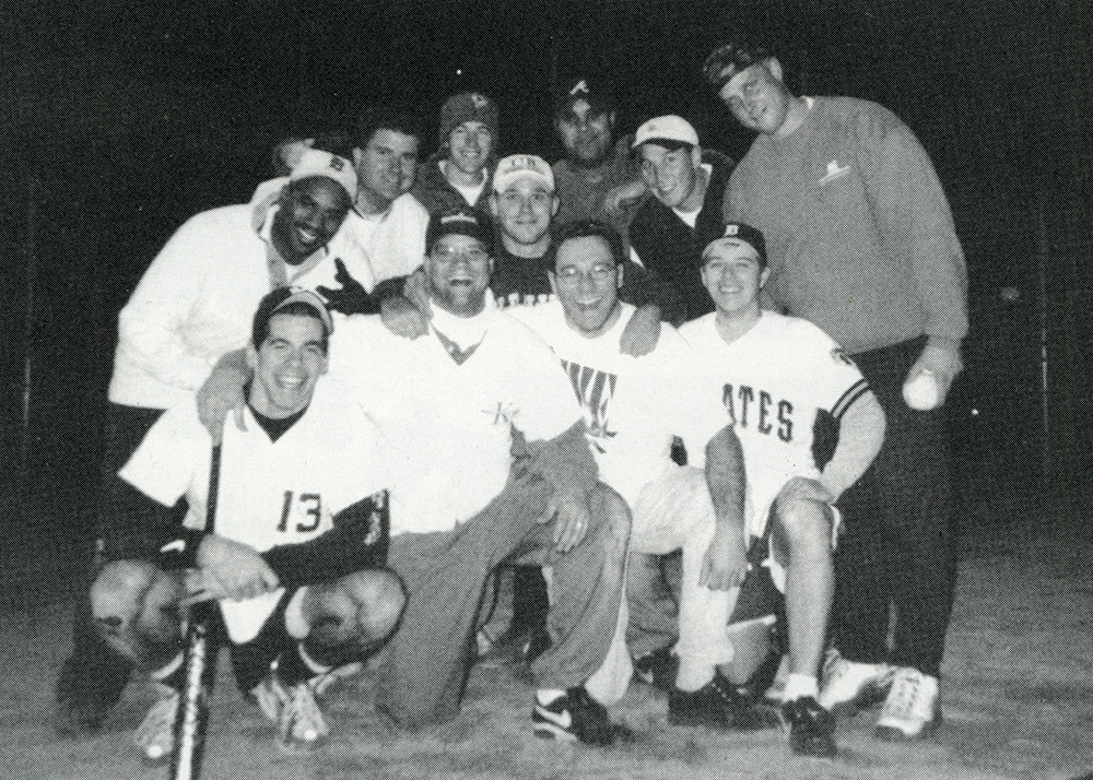 Rob Lynch, wearing a white cap and uniform, poses with nine teammates in a black-and-white photograph of a Simon Business School softball team.