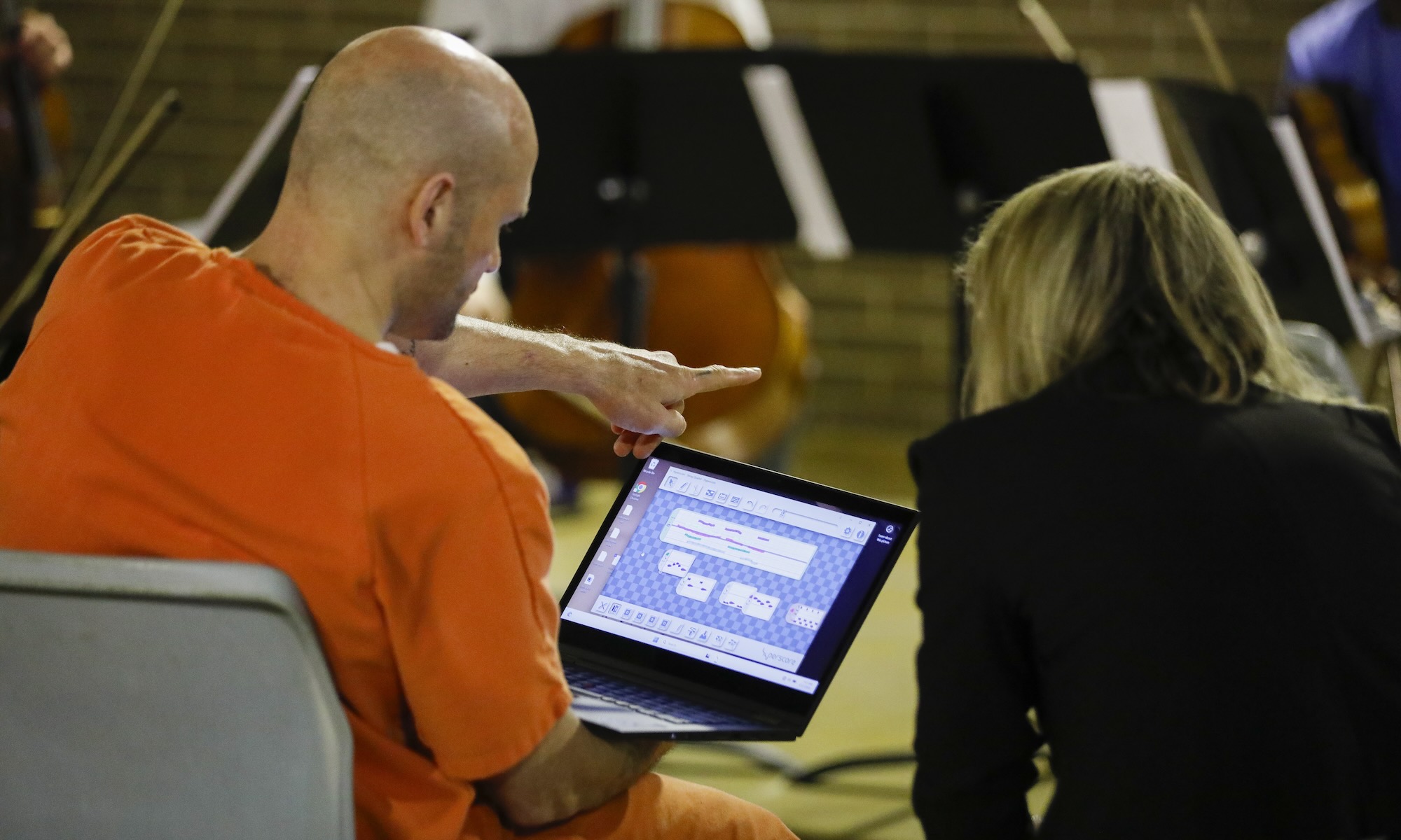 Seen from behind, Elinor Freer helps Monroe County Jail inmate, Josh, compose music on a laptop.