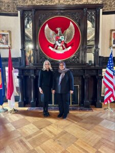 Two women pose for the camera in a government office in front of a coat of arms