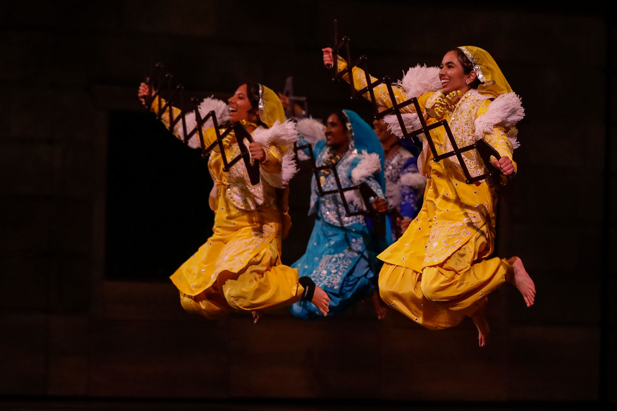 Dancers in traditional costumes perform energetically on stage during a vibrant show at the University of Rochester.