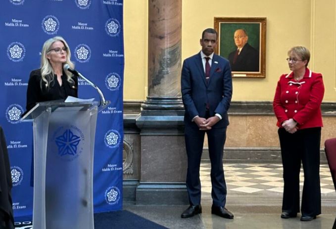 A speaker at a podium giving a speech about two award winners, who are next to them