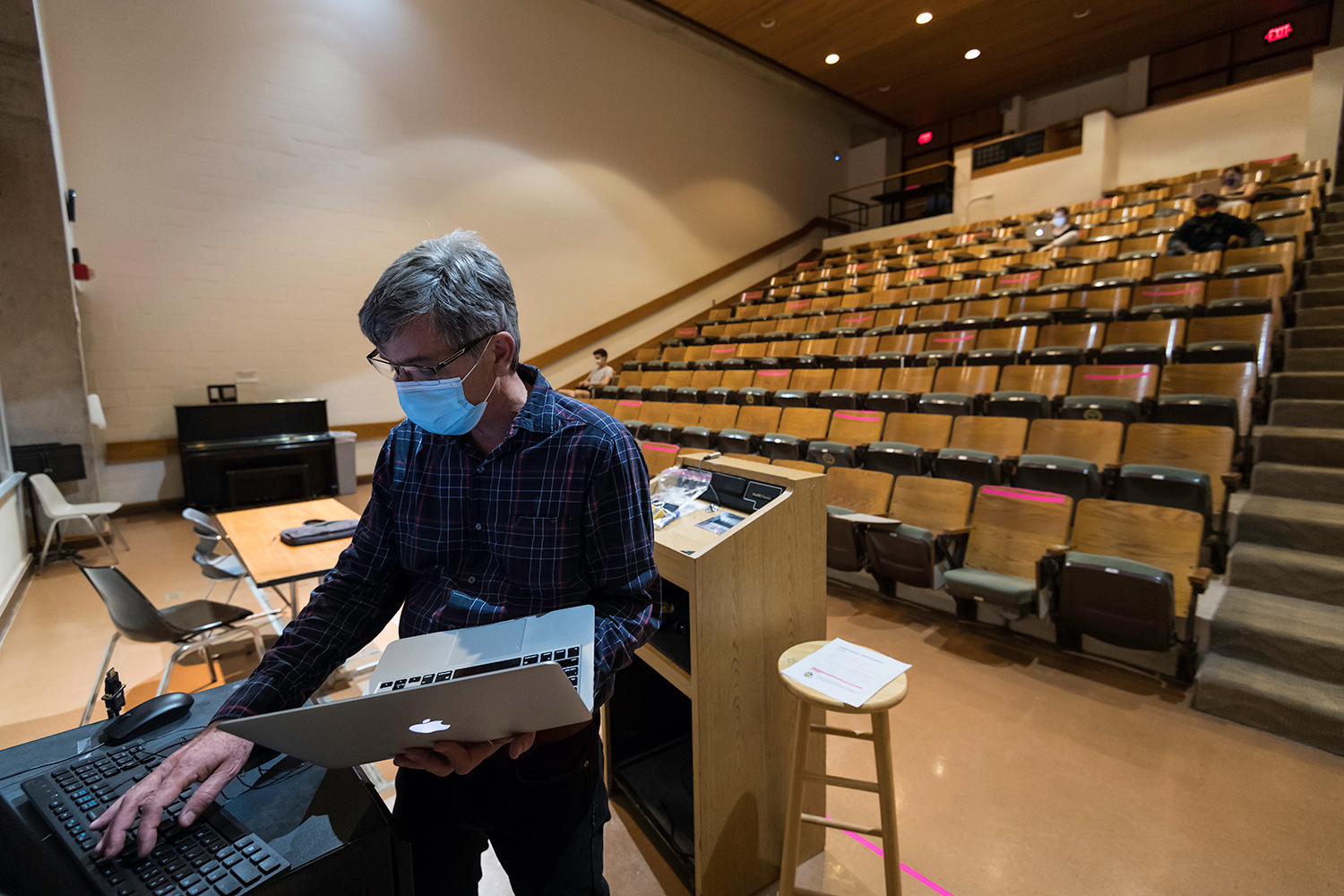 Robert Minckley holds a laptop while working on another computer at the front of a large empty lecture hall.