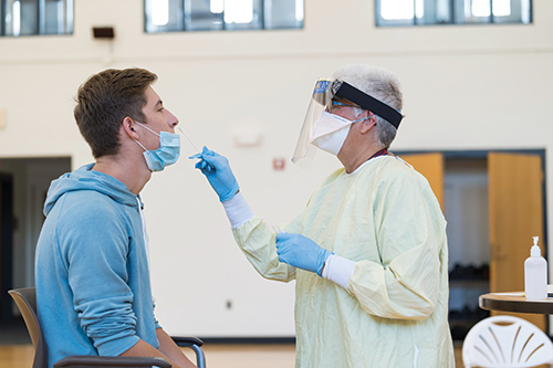 student receives a COVID test through a nasal swab by a nurse in scrubs.