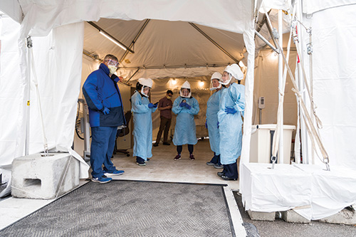 group of health care workers in PPE standing in a medical tent set up in from the hospital.