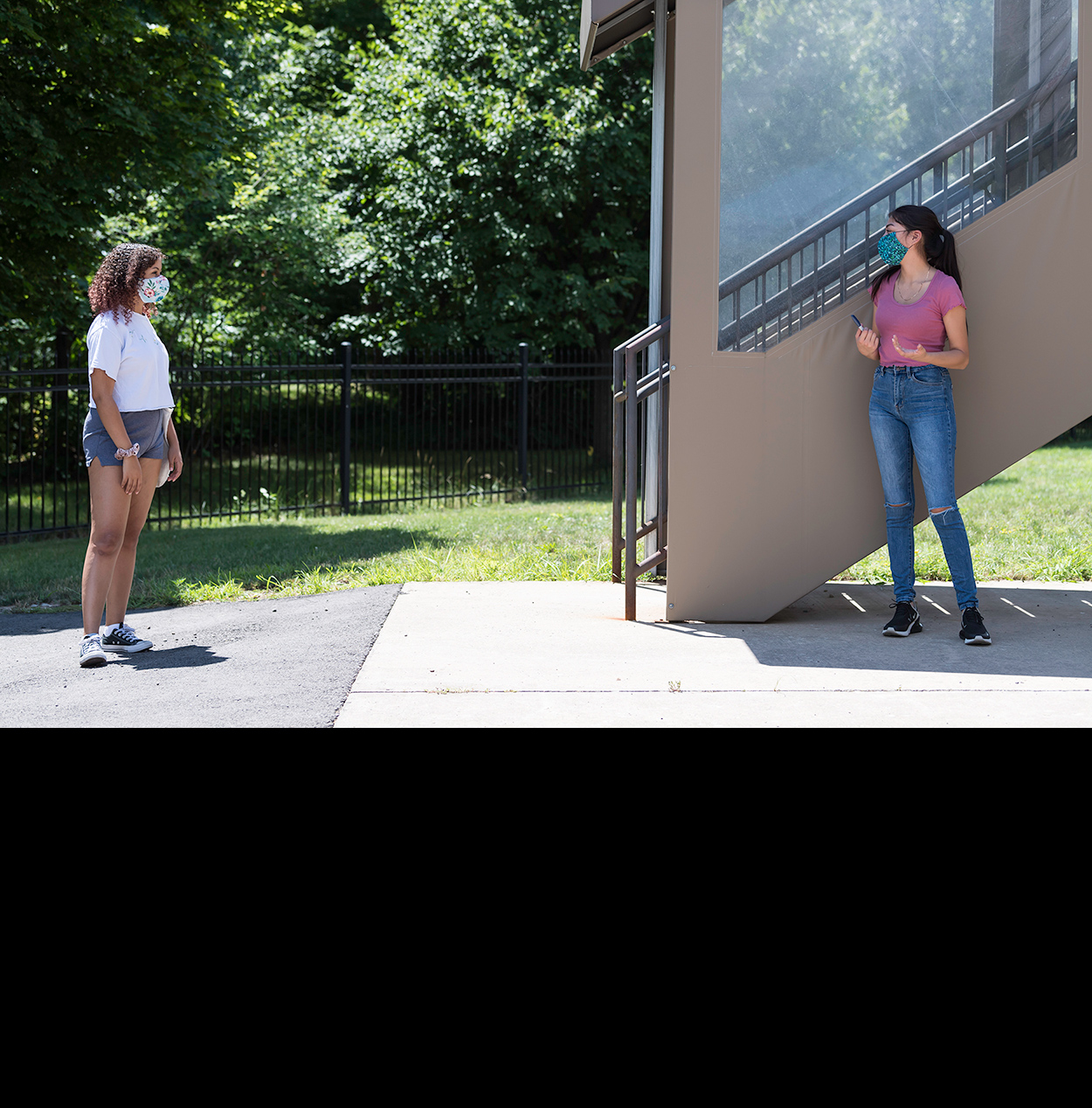 Two students wearing masks, standing more than six feet apart as they wait in line in front of their residence hall.