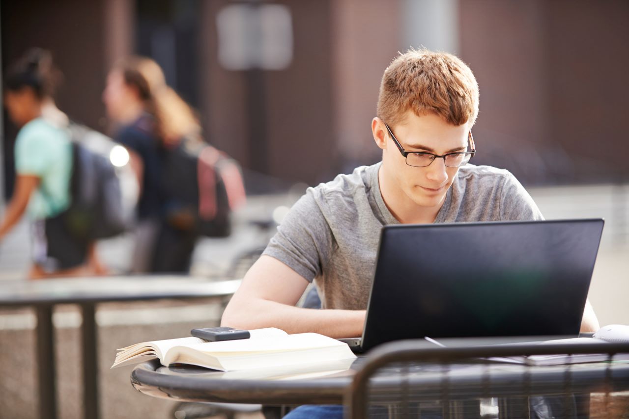 A student working on a laptop outside on a university campus.