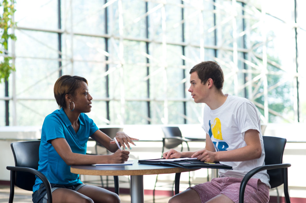 A University of Rochester student and staff member having a conversation at a table