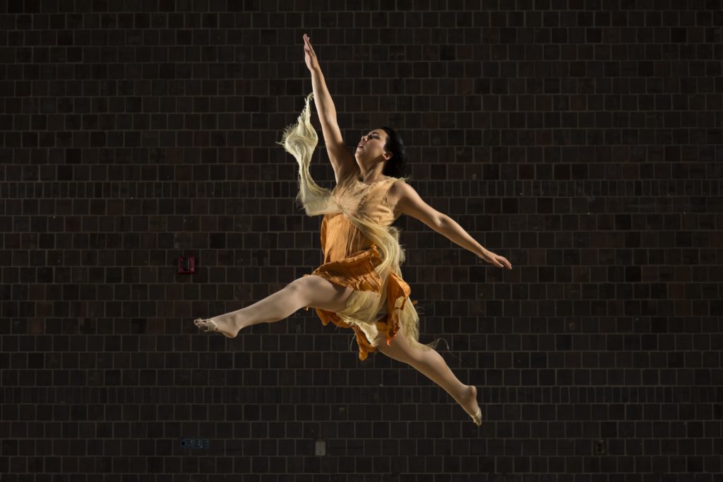 A University of Rochester student dancing on a stage, leaping in mid-air