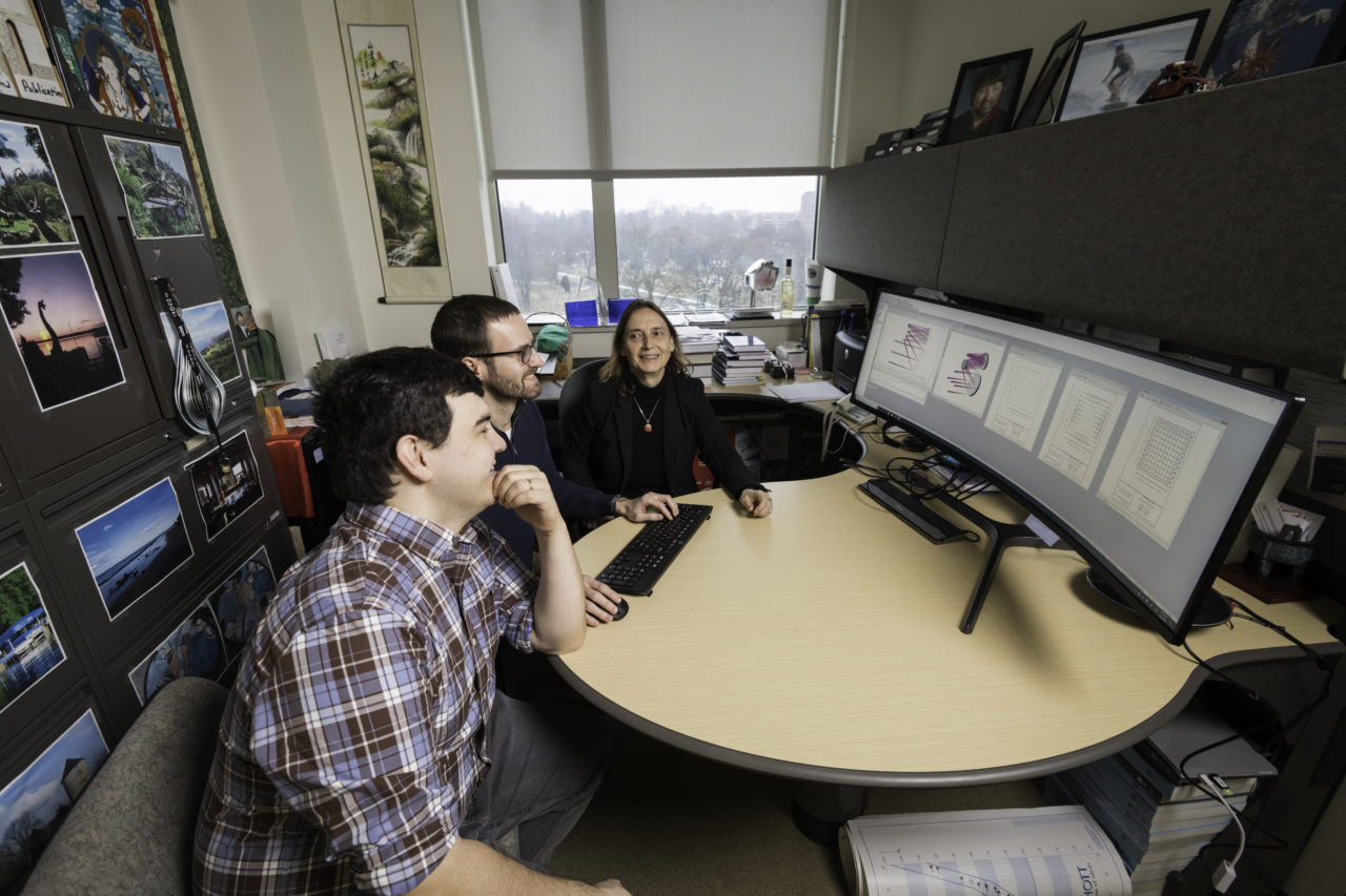 A University of Rochester professor and two students in an office, sitting around a computer with a complicated data set on it