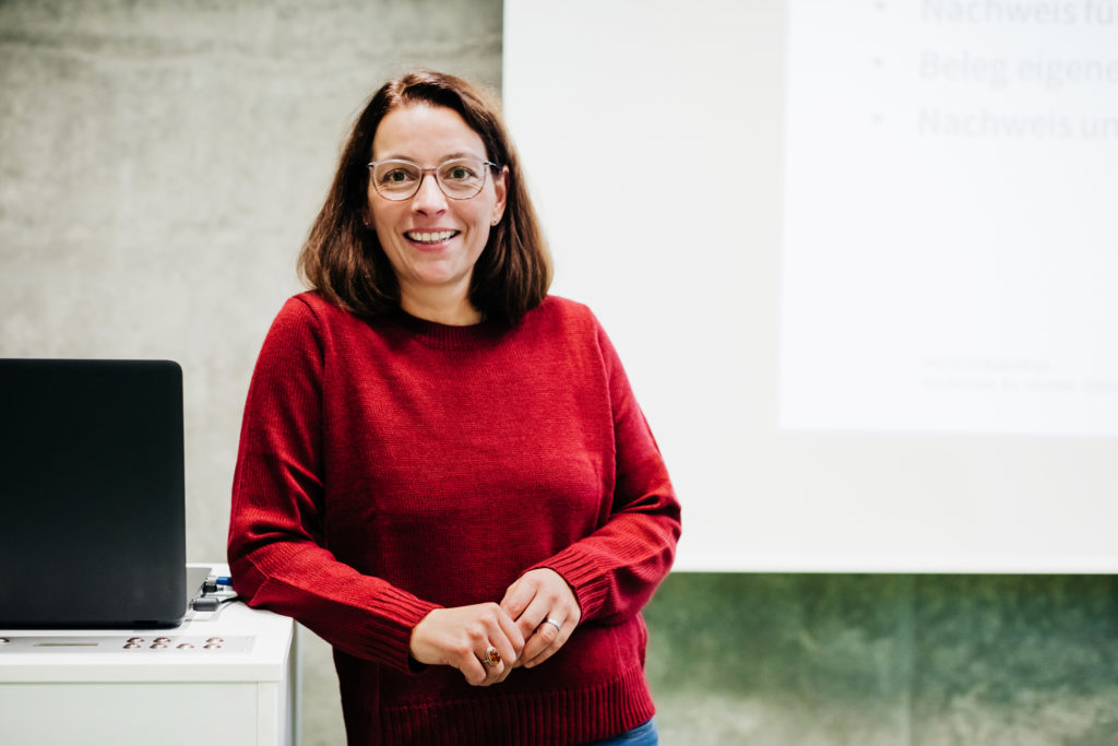 A professor standing at the front of her classroom in front of a chalk board