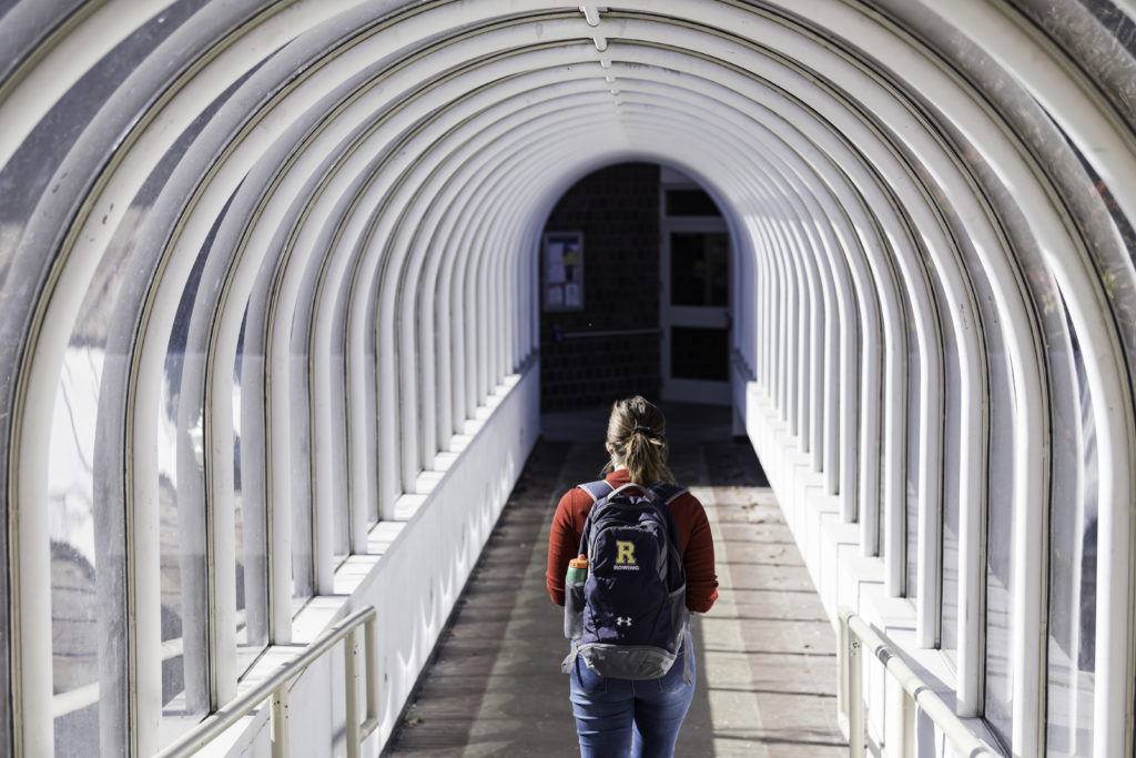 A student wearing a University of Rochester backpack walking through a tunnel on campus