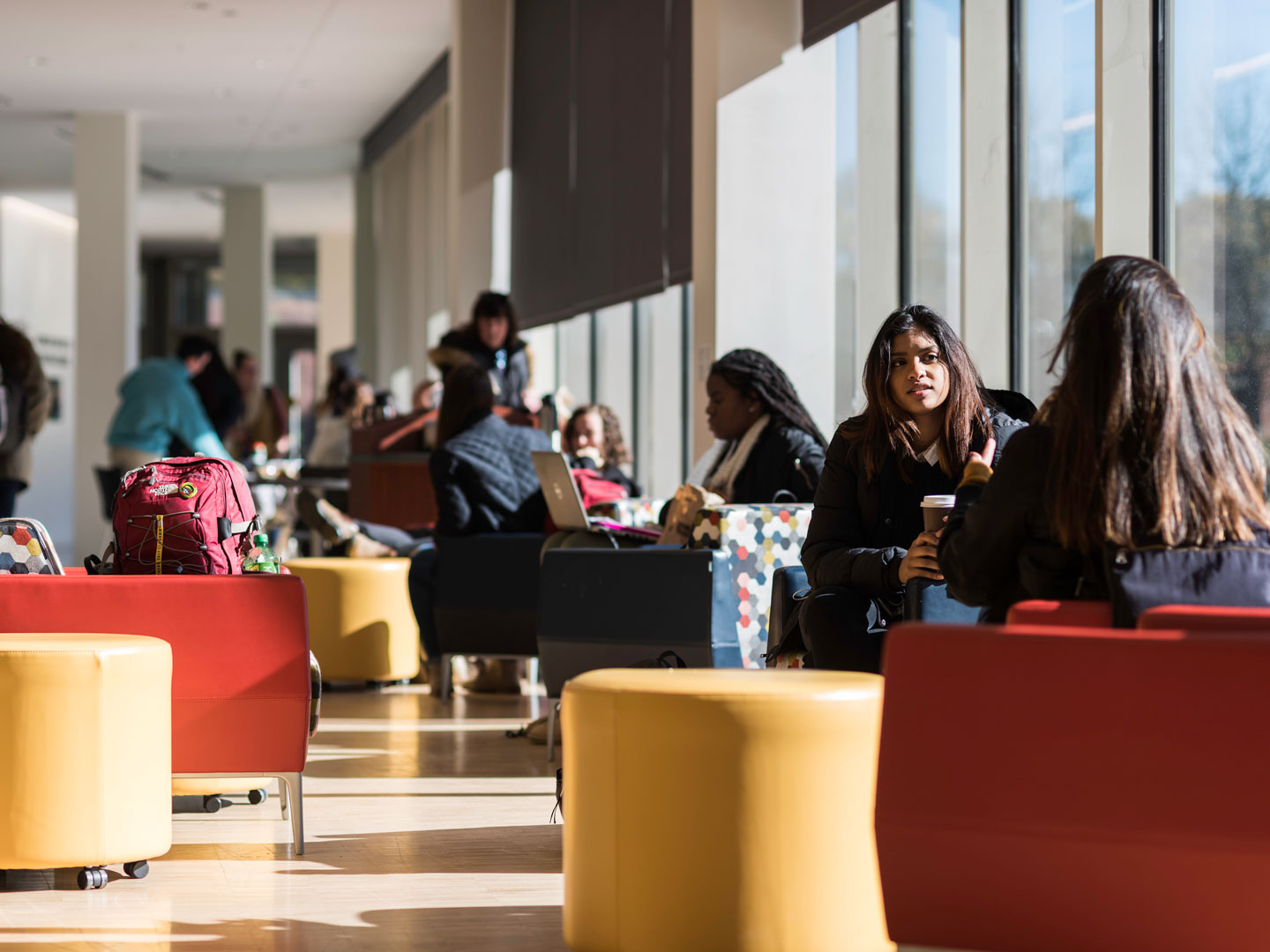 University of Rochester students seated in a spacious, sunlit area with large windows, engaged in study and conversation.