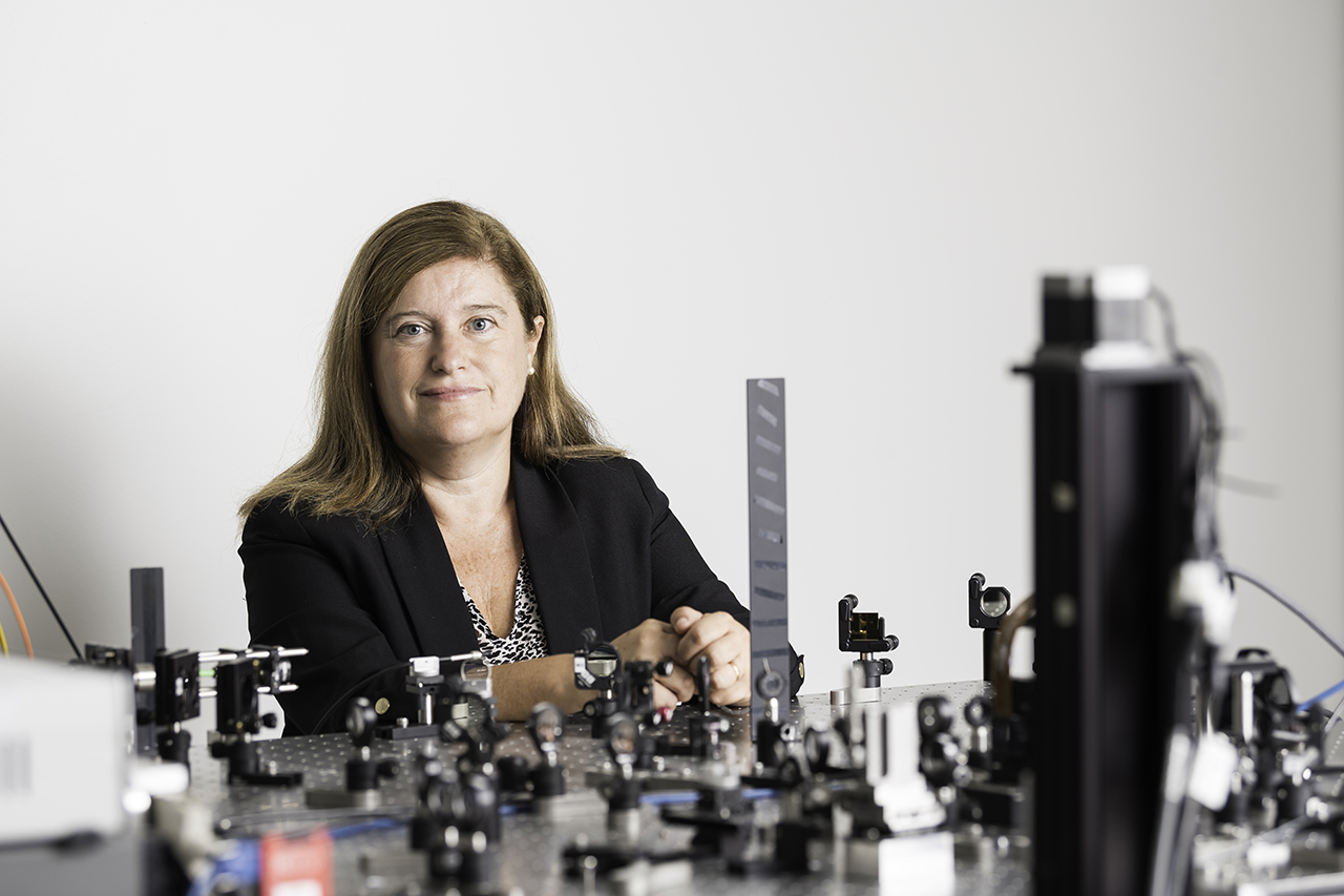 Professor Susana Marcos posing for the camera with an array of lenses in the foreground.