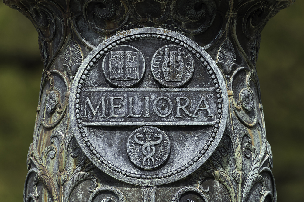 A close up of the Meliora seal on the base of a flagpole on the University of Rochester's Eastman quad.