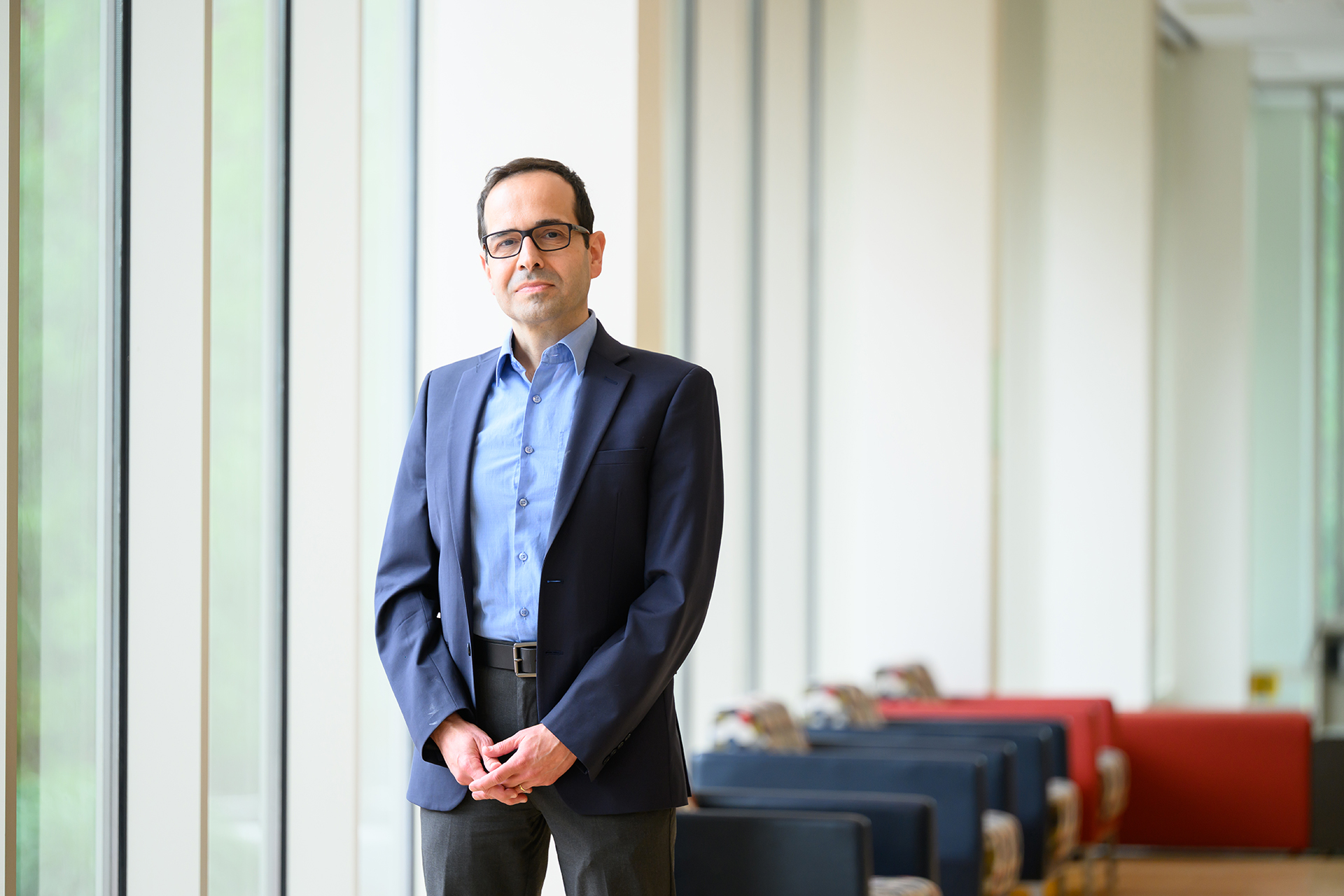 Mujdat Cetin poses for the camera in front of windows with chairs in the background.