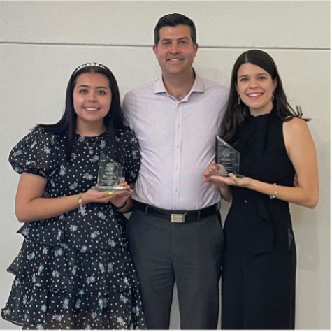 A group of three people smiling at the camera with the outer two people holding awards.